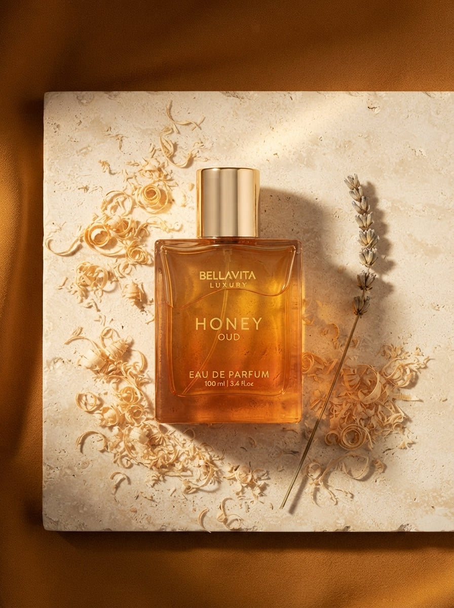 A minimalist perfume bottle on a cream stone surface with wood shavings and a dried flower, set against a warm ochre backgrou